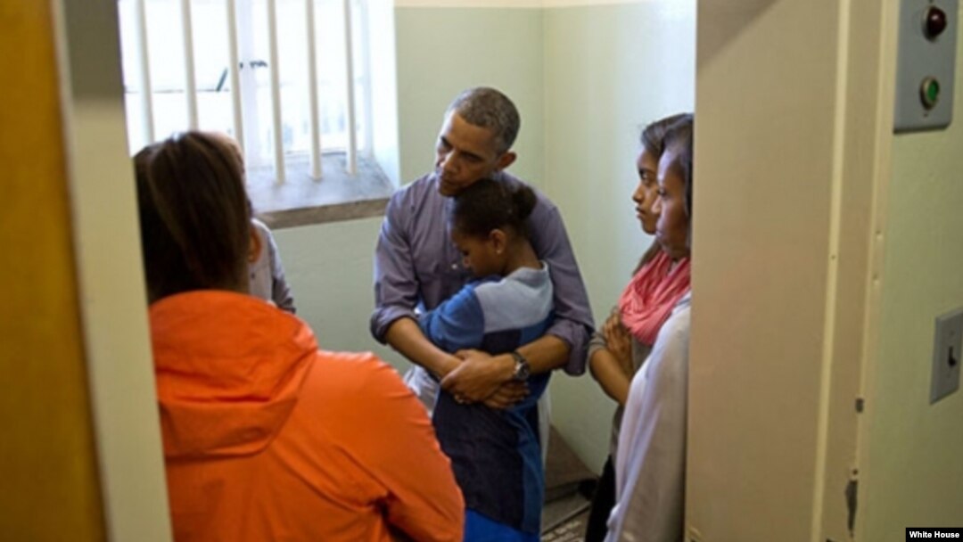 El presidente Obama conforta a su hija menor Sasha, durante la visita a la celda de Mandela en la Isla Robben, junto a su hija Malia y la primera dama Michelle Obama.