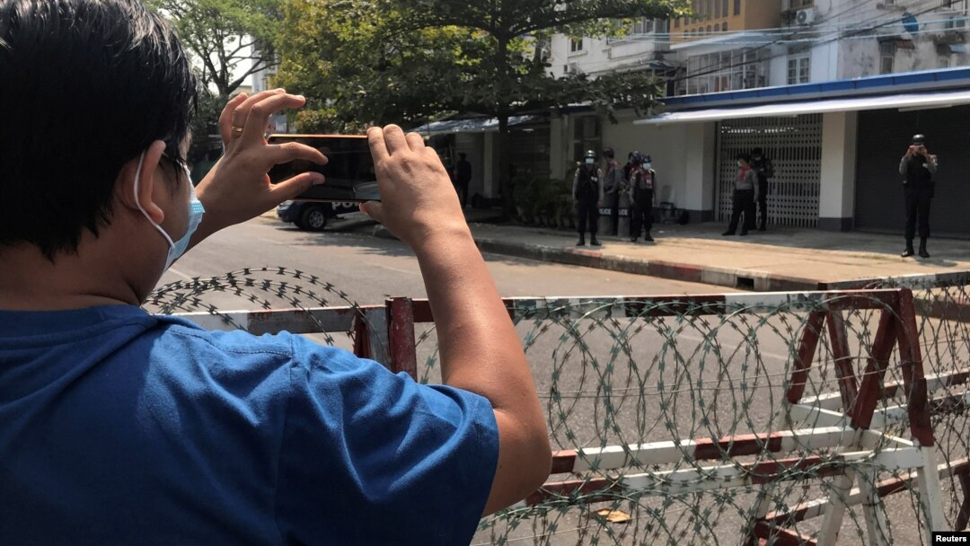 FILE - A journalist and a police officer take pictures of each other during a protest against the military coup, in Yangon, Myanmar, Feb. 23, 2021.