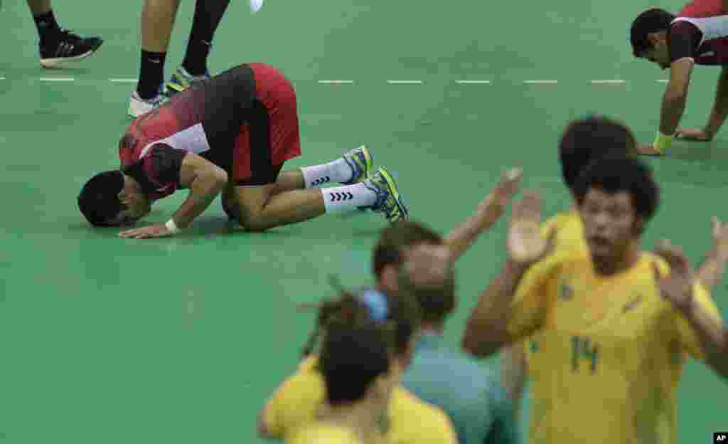 Egypt's Eslam Eissa prays on the court, as Brazil's team celebrate securing a draw, after the men's preliminary handball match between Egypt and Brazil at the 2016 Summer Olympics in Rio de Janeiro, Brazil, Aug. 13, 2016.