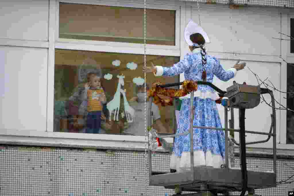 A young patient with relatives watches through a window as a Russian emergency rescue student dressed as Snegurochka (Snow Maiden) perform, outside the Morozov Children's City Clinical Hospital in Moscow.