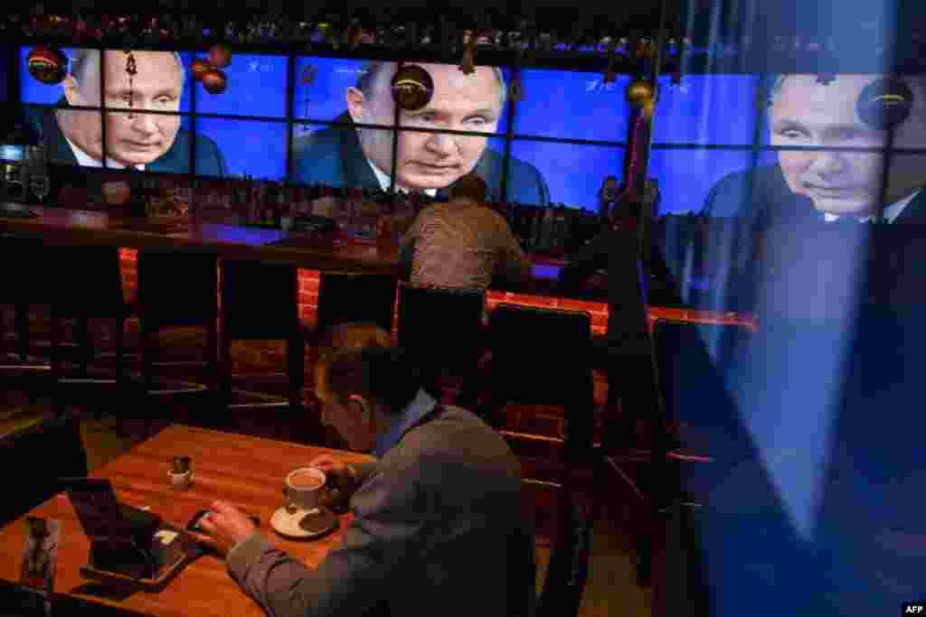 A man drinks a coffee in front of screens broadcasting Russian President Vladimir Putin's annual press conference, at a bar in Moscow, Russia.