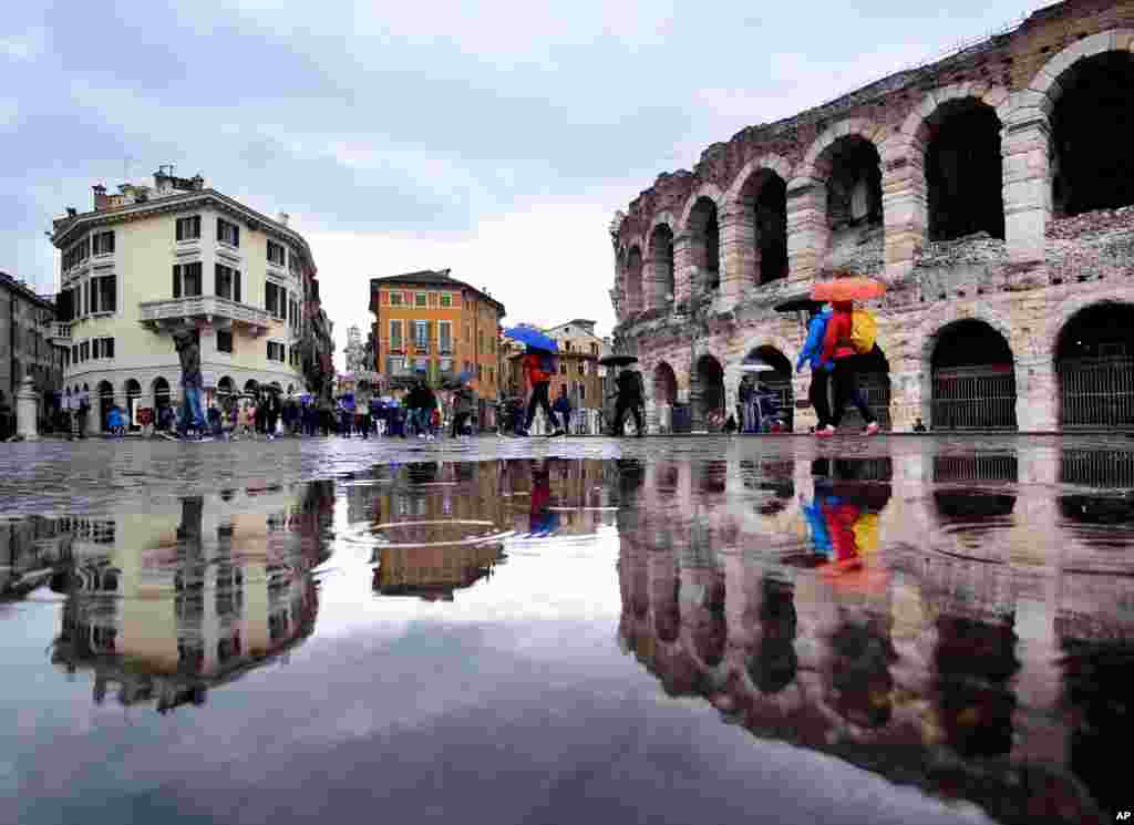 Tourists walk in the rain along the old arena, right, and past the buildings of the old town in Verona, Italy.