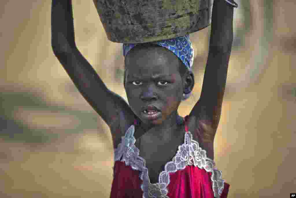 Uma menina transporta na cabeça uma bacia de água para o seu abrigo improvisado no campo de refugiados das Nações Unidas, que é agora a casa de milhares de pessoas deslocadas de guerra, resultante do conflito que eclodiu em Jebel, arredores de Juba. Dez. 31 2013.