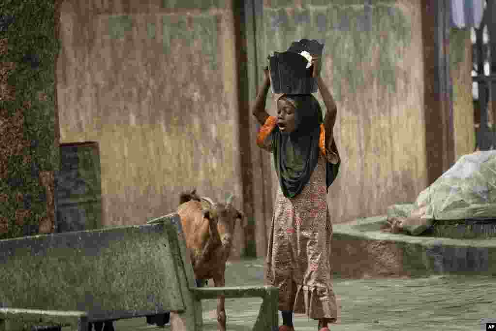 A young girl carrying a broken plastic bucket full of food on her head in Kano, northern Nigeria.