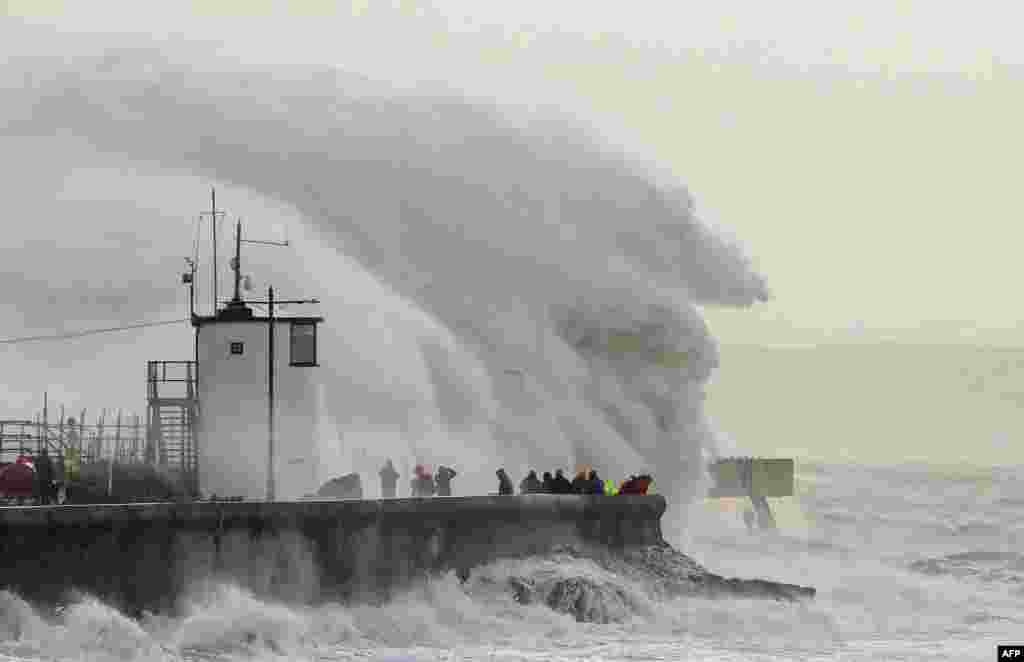 People watch as waves crash against the sea wall at Porthcawl, south Wales, as Storm Eunice brings high winds across the country.