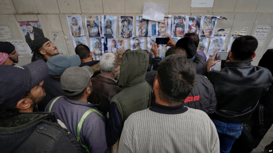 FILE - People examine photos as they search for missing or deceased people on the wall outside the morgue of Al-Mojtahed Hospital in Damascus, Syria, Dec. 11, 2024. 