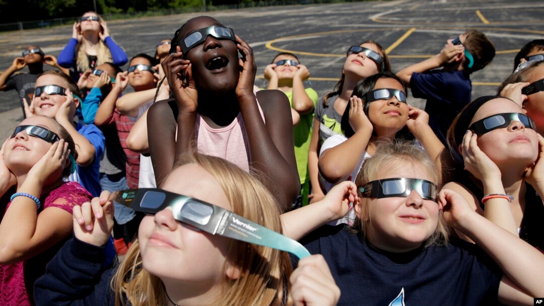 In this photo taken Friday, Aug. 18, 2017, fourth graders at Clardy Elementary School in Kansas City, Mo. practice the proper use of their eclipse glasses in anticipation of Monday's solar eclipse. (AP Photo/Charlie Riedel)