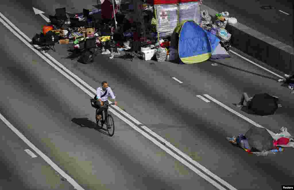 A man rides his bicycle to work along an area blocked by protesters at the main street to the financial Central district outside of the government headquarters building in Hong Kong, Oct. 6, 2014.