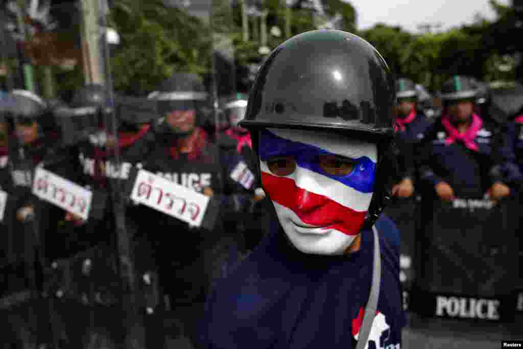 An anti-government protester wearing a mask painted in the colors of the Thai national flag looks on as riot police officers stand guard outside the parliament in Bangkok. Thailand's parliament was due to debate a political amnesty bill as anti-government protesters marched to try to get it scrapped, saying it could let ex-premier Thaksin Shinawatra return from exile without having to serve a jail sentence.