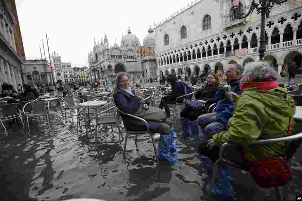 Tourists enjoy an ice-cream as they sit in flooded St. Mark's Square in Venice, Italy.