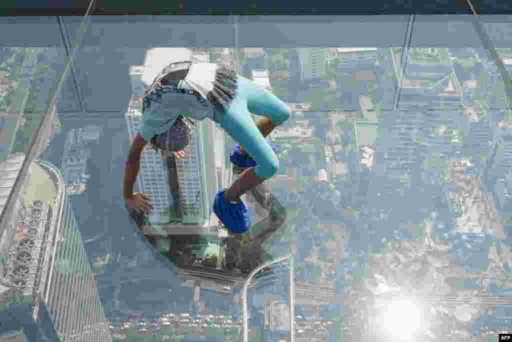 A girl plays on the glass skywalk on the 78th floor of the King Power Mahanakhon skyscraper, Bangkok's highest observation deck, Thailand.