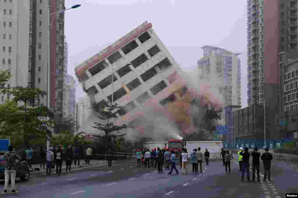 People watch the controlled demolition of an eight-storey "nail house" that stood on a road in Haikou, Hainan province, China.