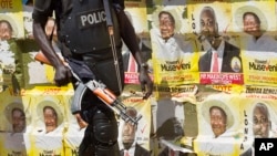 FILE - A Ugandan policeman is seen on patrol against the backdrop of numerous campaign posters for long-time President Yoweri Museveni, on a street in Kampala, Uganda, Feb. 17, 2016.
