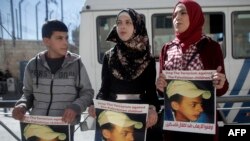 FILE - Relatives of Palestinian teenager Mohammed Abu Khdeir who was killed in 2014, hold posters bearing his portrait outside the Jerusalem district court during a hearing on Feb. 4, 2016. 