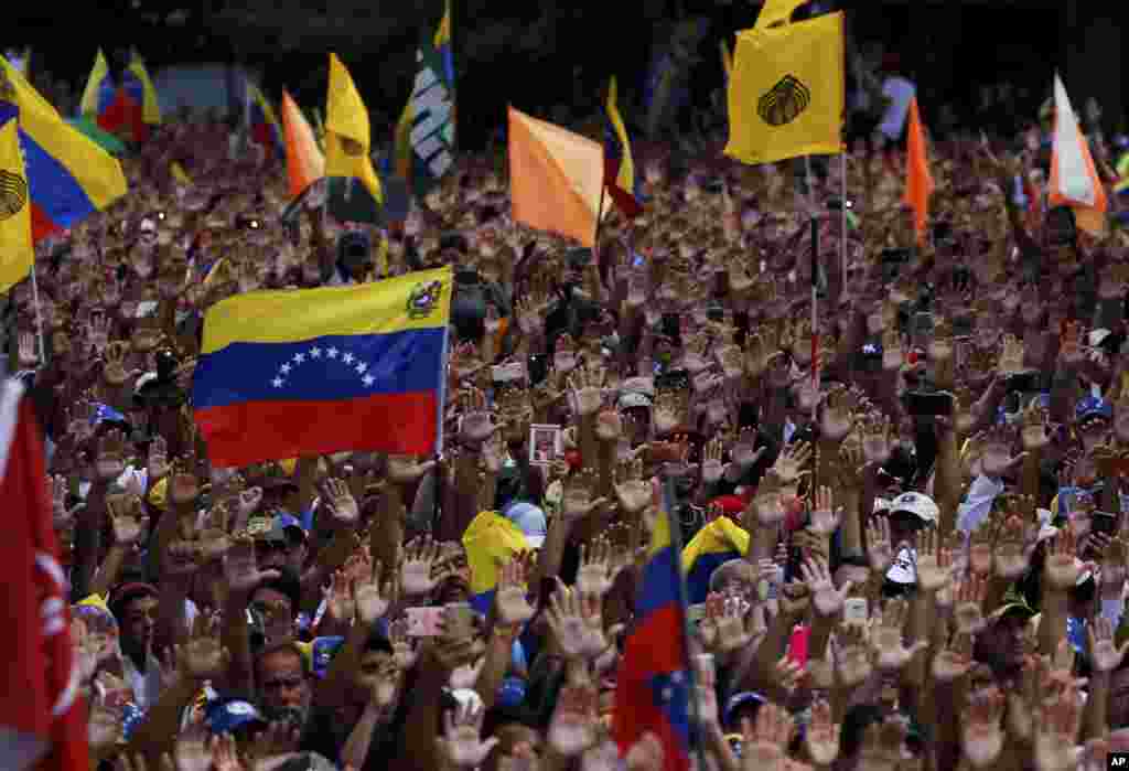 Anti-government protesters hold their hands up during the symbolic swearing-in of Juan Guaido, head of the opposition-run congress who declared himself interim president of Venezuela during a rally demanding President Nicolas Maduro's resignation in Caracas.