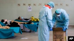 Paramedics carry an hazardous medical waste box as patients lie on camping beds, in one of the emergency structures that were set up to ease procedures at the Brescia hospital, northern Italy, Thursday, March 12, 2020. (AP Photo/Luca Bruno)